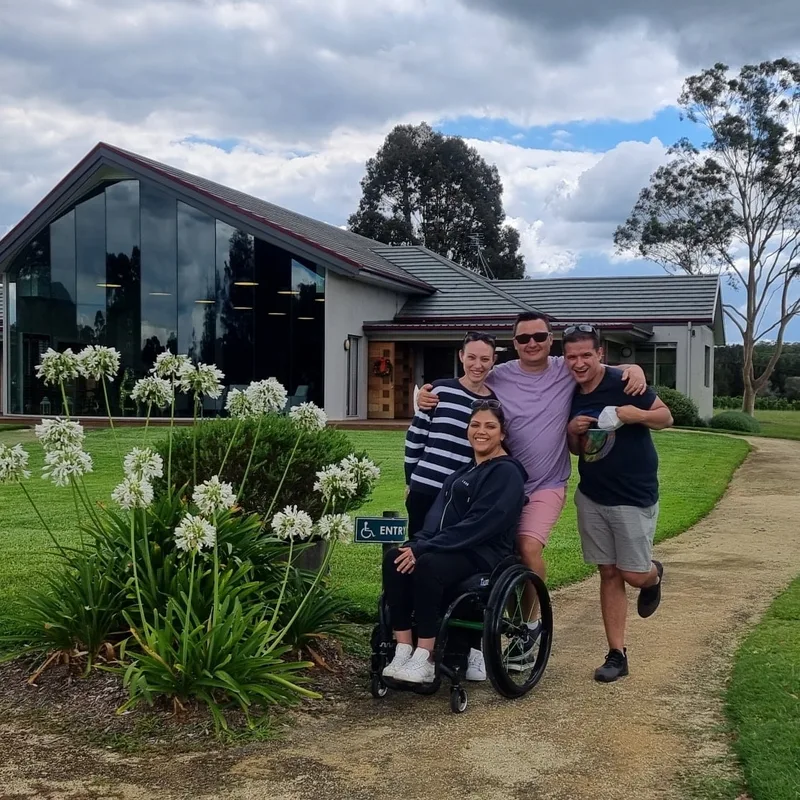Four friends, one using a wheelchair, in front of a modern cellar door