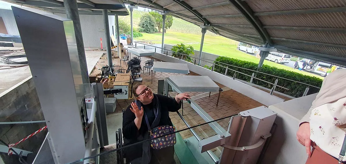 A guest waves from the hydraulic lift of the HV Tours accessible minibus