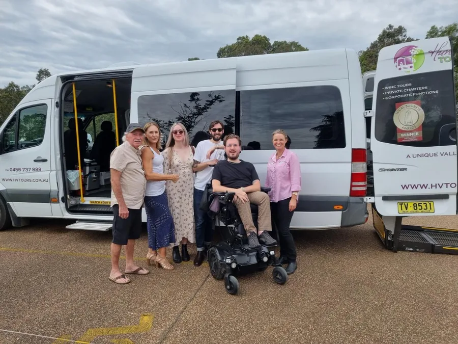 A tour group, one guest in a wheelchair, in front of two Hunter Valley Tours vans