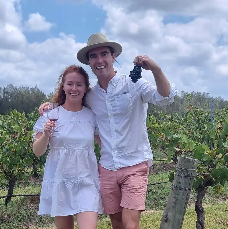 A couple in the vineyard with a bunch of grapes and a glass of red