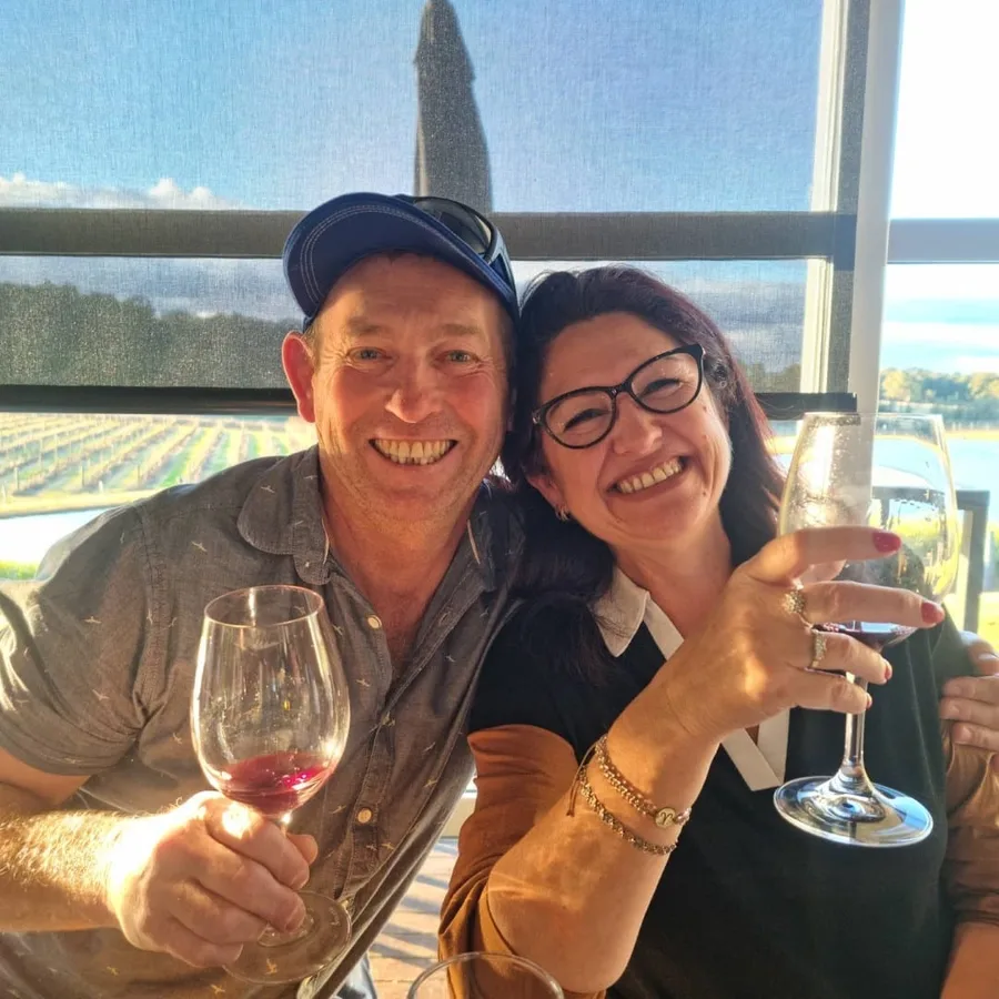A couple toasts with red wine in front of a vineyard view