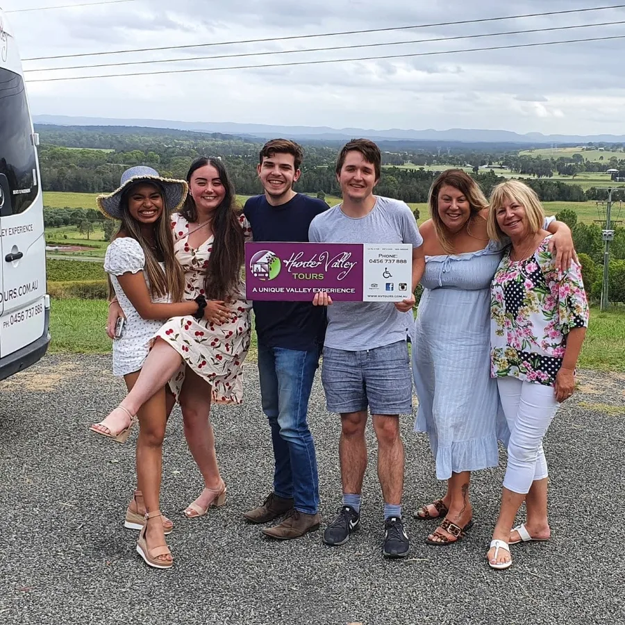 A family holds the Hunter Valley Tours sign above a valley lookout