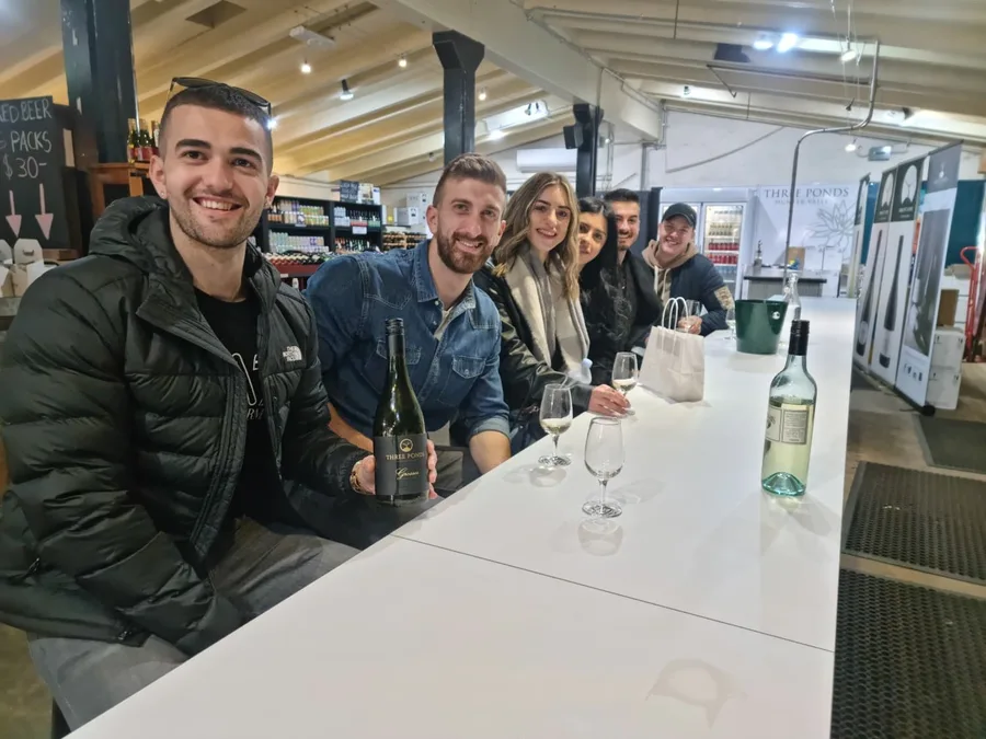 Guests seated along a white cellar door tasting bar, wine bottles and glasses on the counter