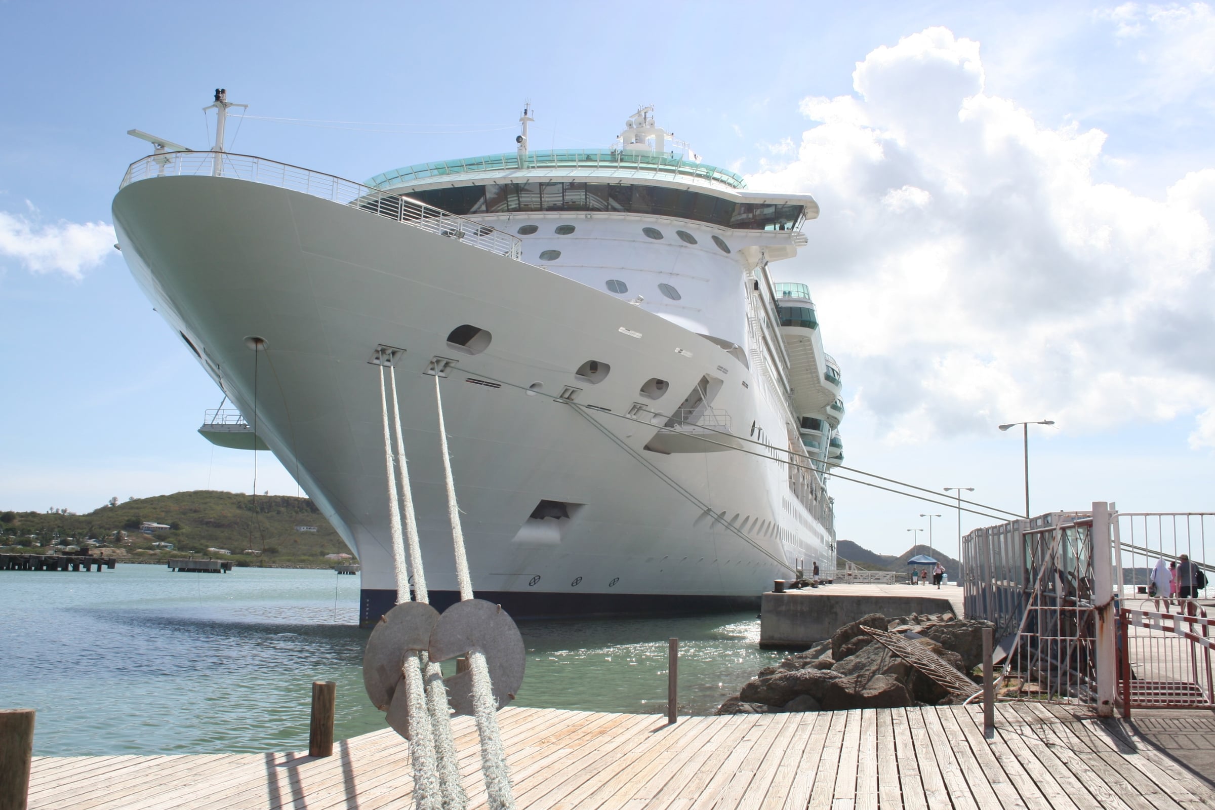A large white cruise ship docked at a pier, viewed from a low angle.